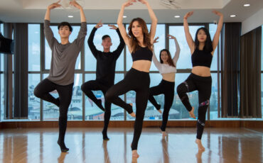 Group of slim Asian people standing on one foot and looking away while dancing in stylish studio